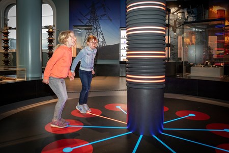 Two children stand on lit-up circles on the floor of an interactive installation.
