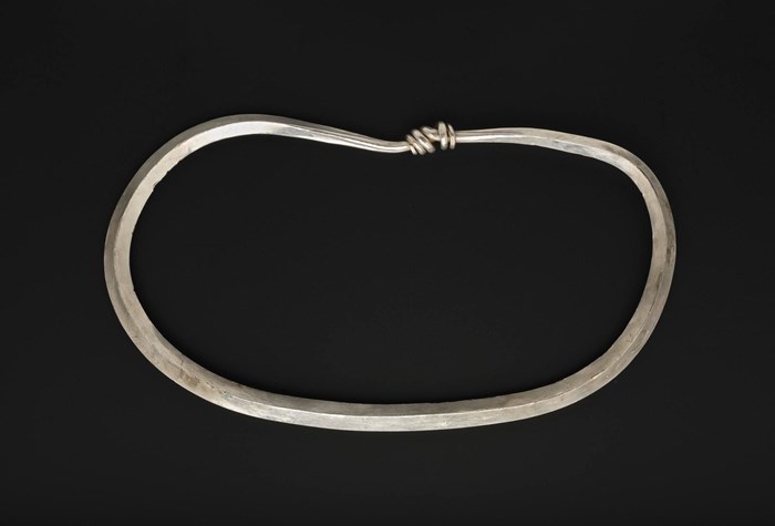 A thin, undecorated, smooth-surfaced silver arm ring coiled in a loop against a black background.