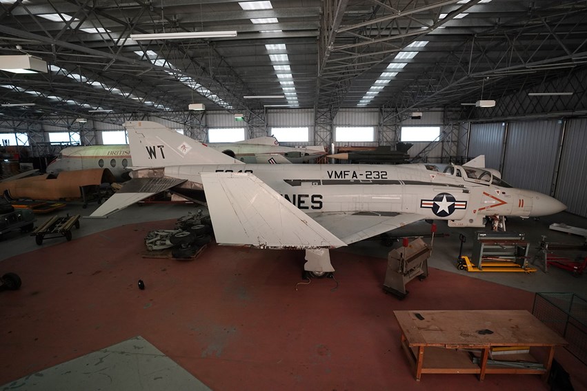 A large grey aircraft with folded wings inside a storage hangar.