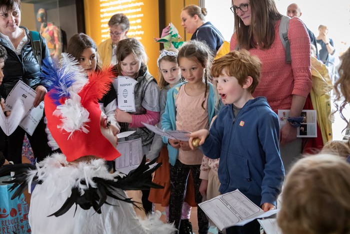 Children looking amazed by performers in feathered costumes.