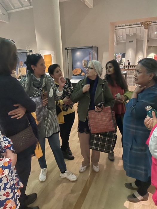 A group of six women standing in a gallery space having a conversation.