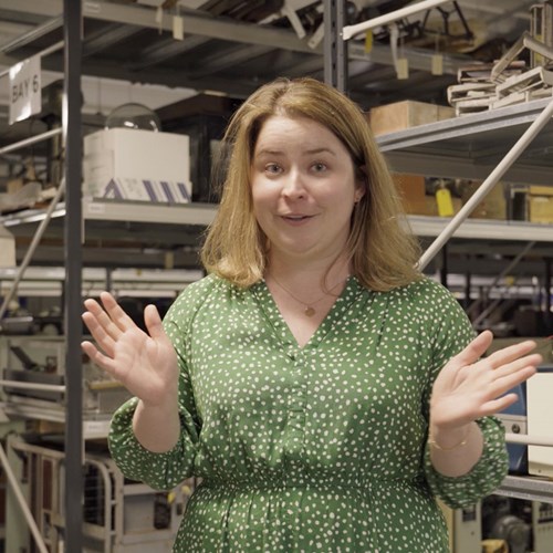 Sophie Goggins stands in front of shelves of science objects.