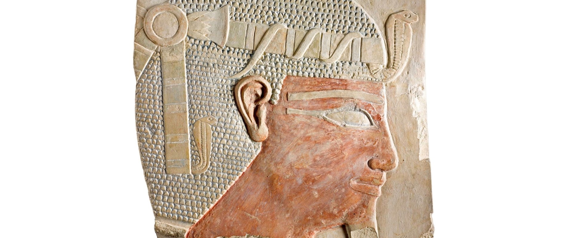 Relief on limestone showing the crowned head of a male Egyptian ruler. His hair is densely patterned with small triangles, and his crown has a cobra at the front.