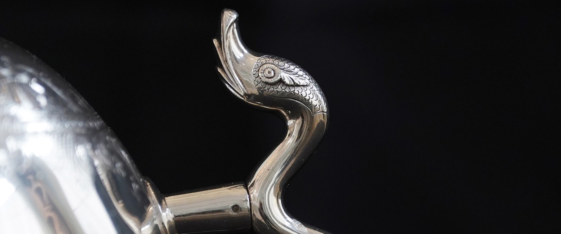 Closeup of the handle of one of the ovoid urns and a small portion of the urn's body. The handle is extremely thin and wavy, its top end shaped to resemble a serpent's head.