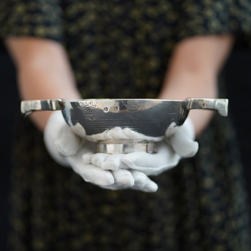 Closeup of a silver quaich being cradled in a woman's white-gloved hands.