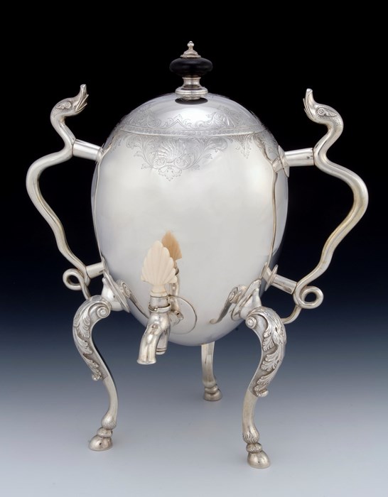 Silver coffee pot shaped like an egg, held up on three curved silver legs and with two long, thin handles made to look like serpents. A pouring spout is near the bottom of the egg-shaped vessel.