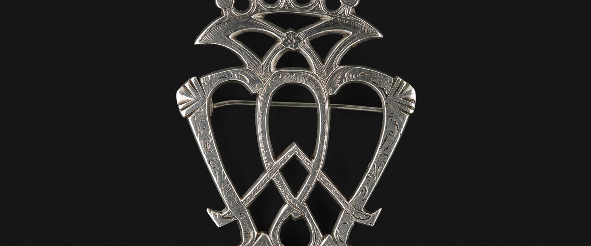 Detail of a silver heart brooch, highlighting the criss-crossed bars and crown-like top section.