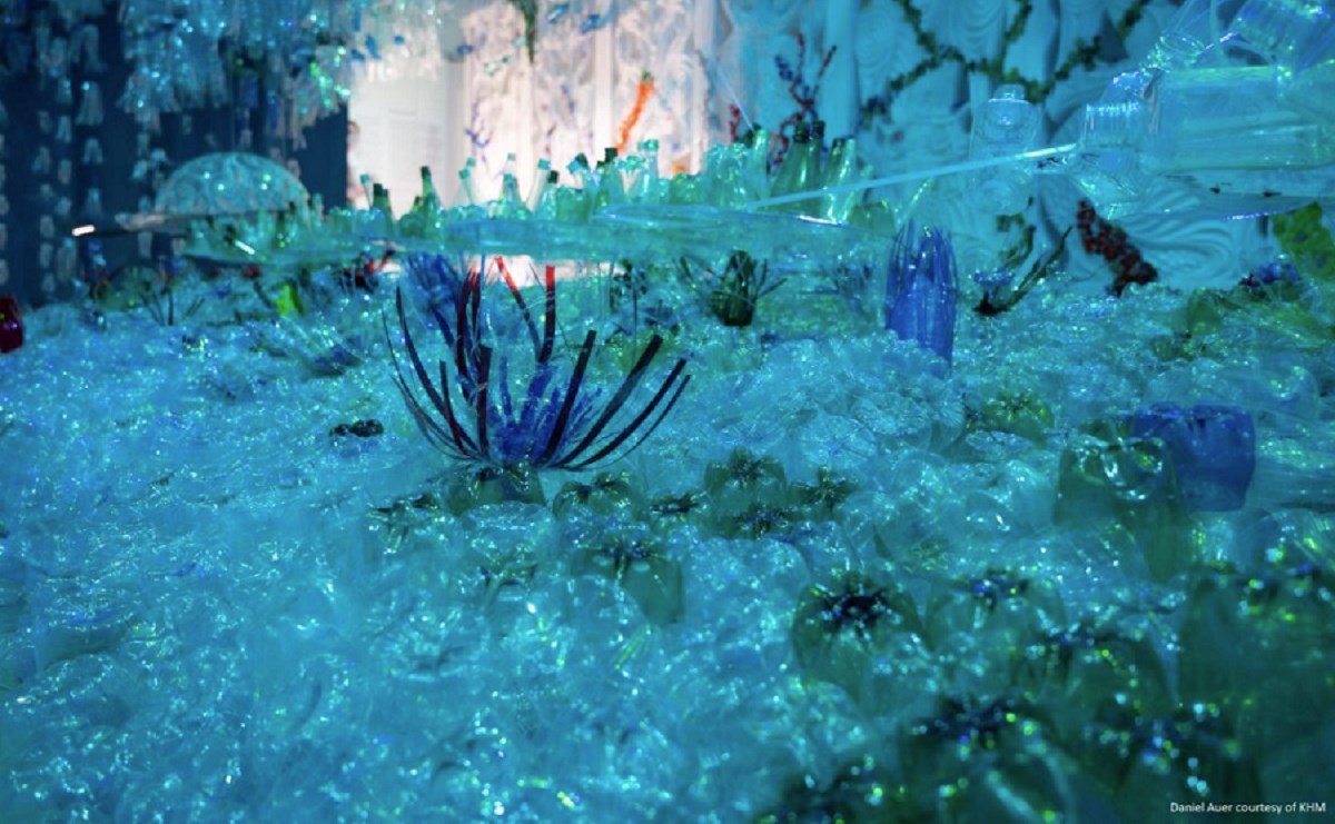 A museum display replicating a vibrant, bright blue sea floor, but with everything made from plastic - plastic bottle jellyfish, plastic padding on the floor, and plastic straws forming anemones.