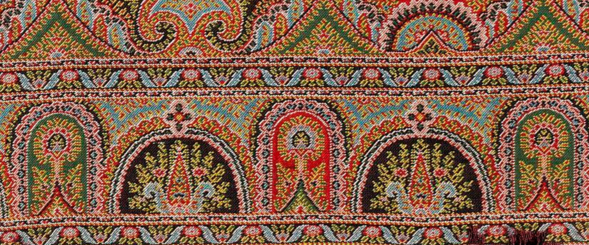 Paisley shawl pattern, short length of a woven border with long cone or buta shapes at the centre, detailed multi-coloured design predominantly in shades of red, blue and green.