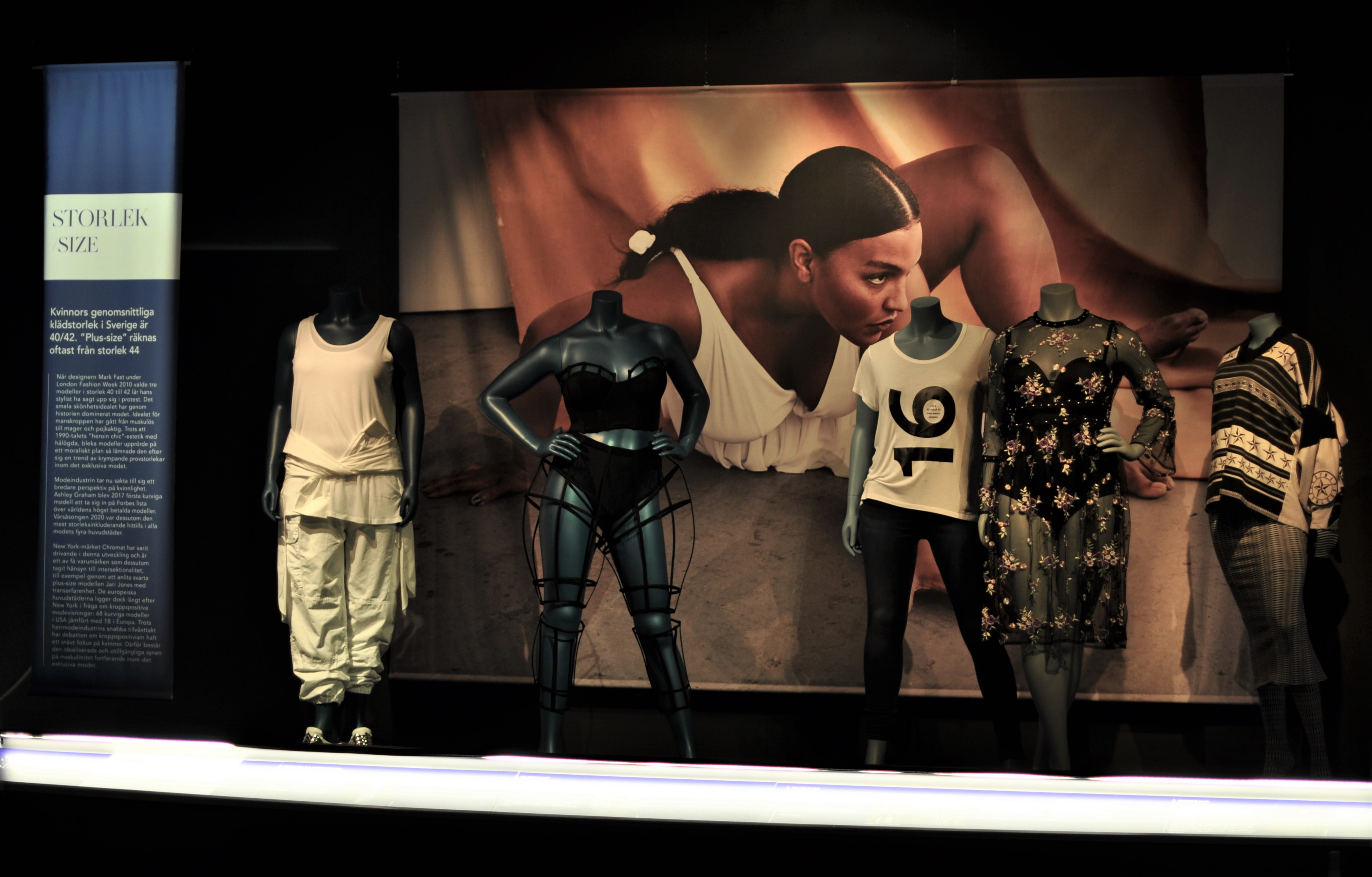 Five mannequins styled against exhibition backdrop. 