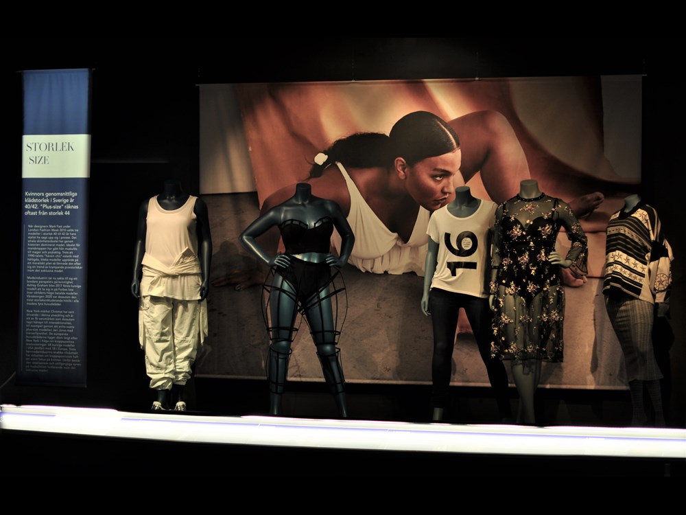 Five mannequins styled against exhibition backdrop. 