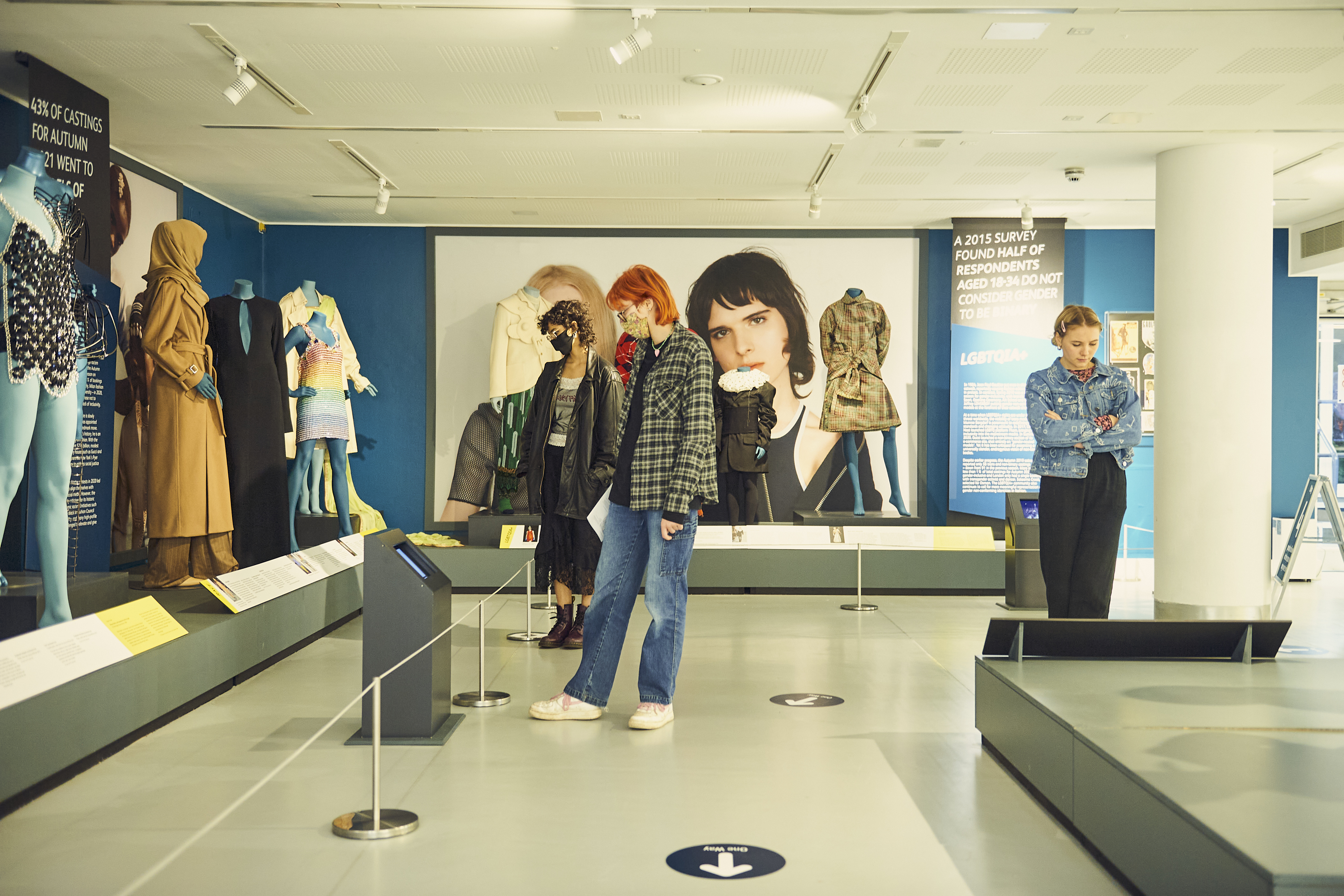 Three visitors in face-masks look at a selection of styled mannequins within the exhibition.
