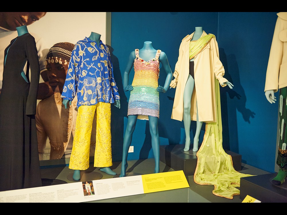 Three styled mannequins within the exhibition pose in garments of a variety of yellow and blue colours.