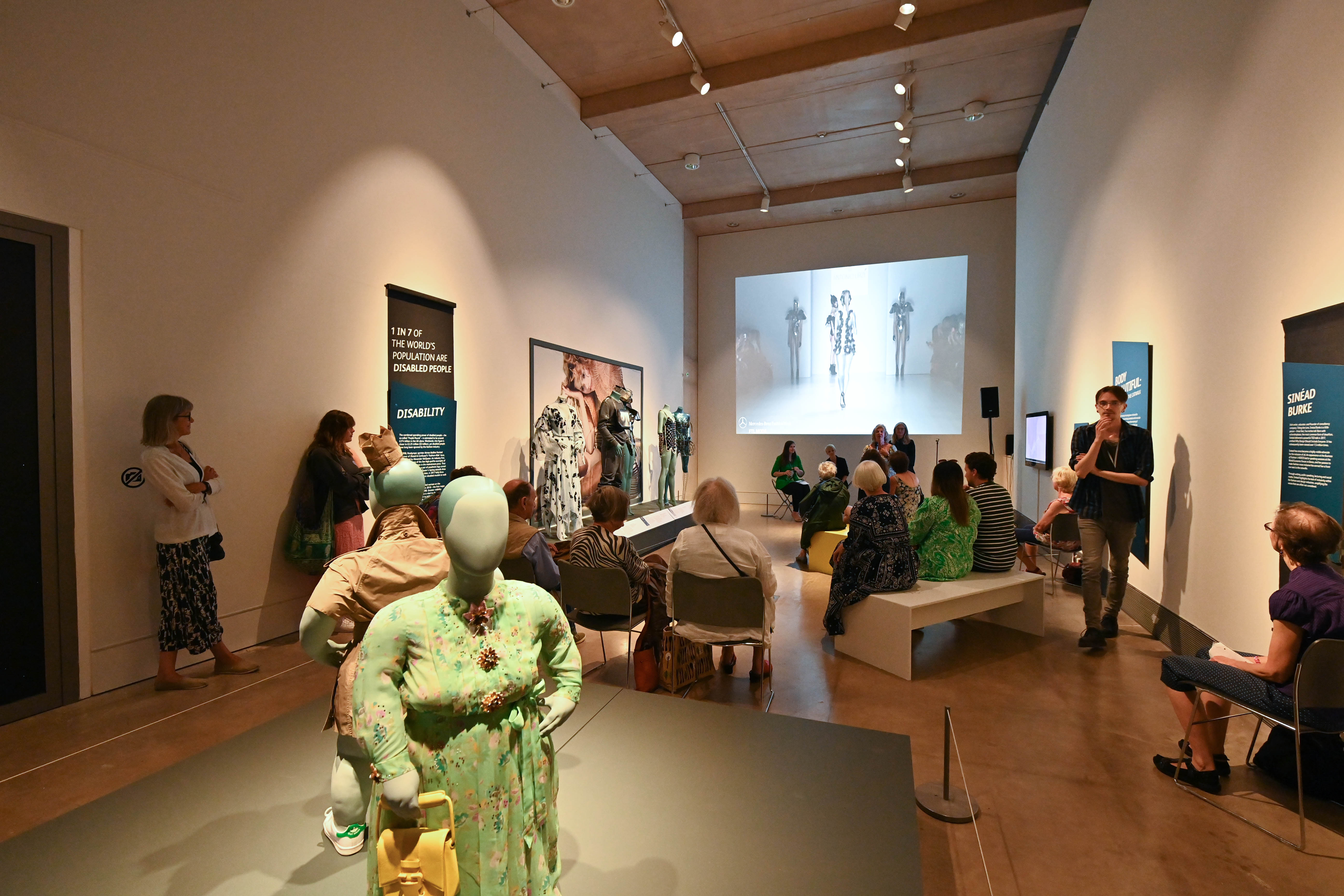 A group of people attend a talk within one of the gallery spaces during the exhibition.