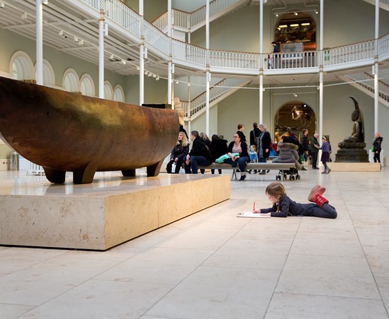 A child lies on floor drawing the umete or feast bowl in the Grand Gallery at the National Museum of Scotland.