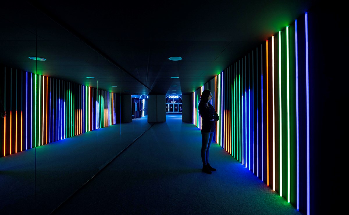 A visitor looks at a brightly lit neon wall, in Game On at Fundación Canal.