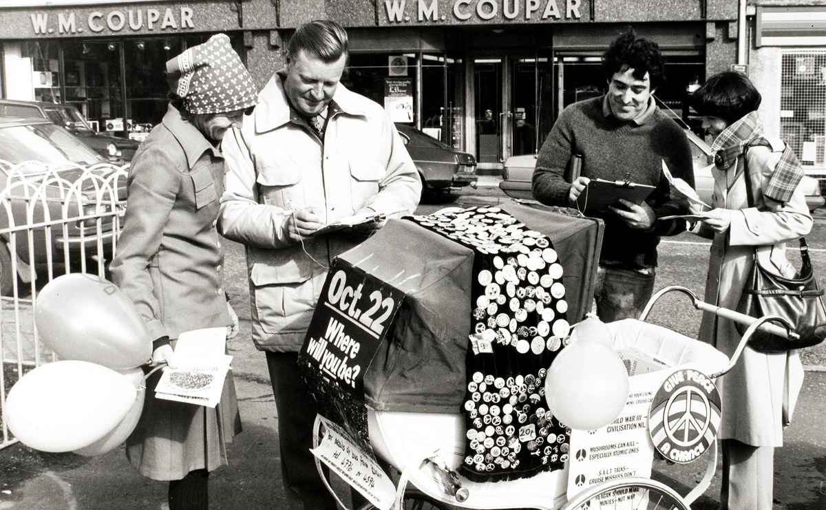 Four people gather around a pram covered in homemade badges.