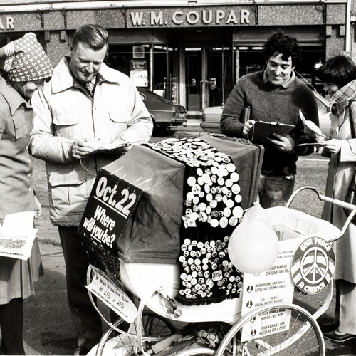 Four people gather around a pram covered in homemade badges.