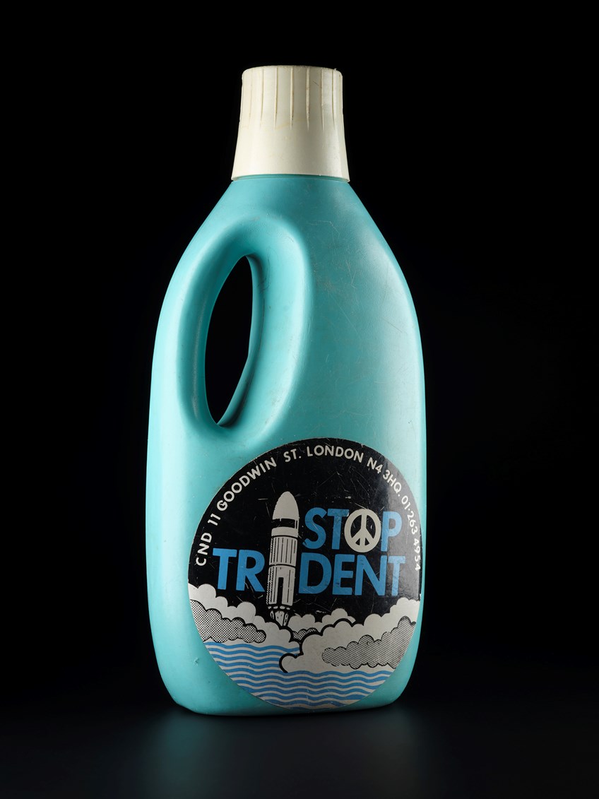 A blue detergent bottle with a large sticker that reads 'stop trident'