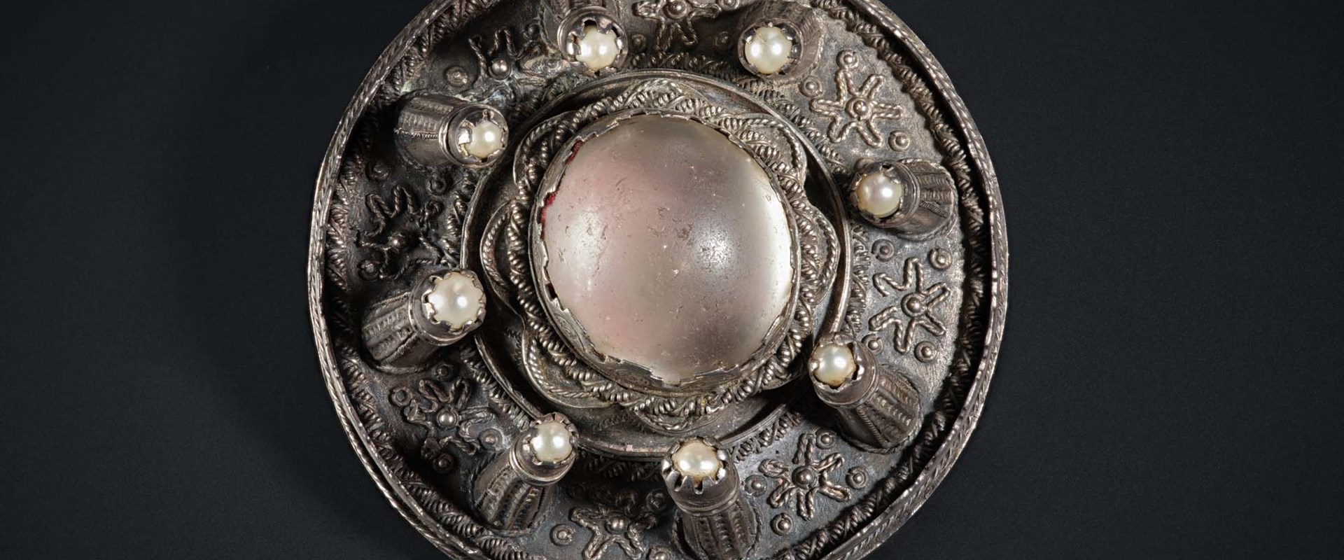 A circular metal brooch with raised decorative elements.
