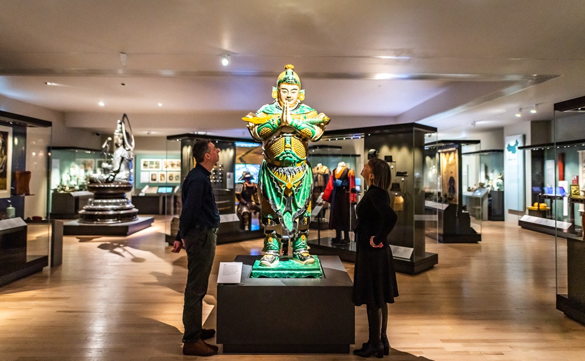 Two people in a gallery looking up at the figure of the bodhisattva Weituo in the East Asia gallery.