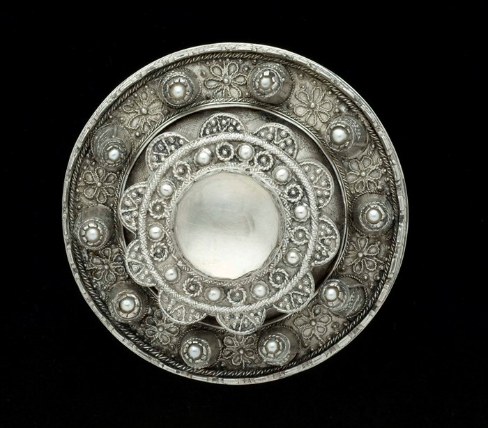 A circular silver brooch with decorated with crystals and pearls.