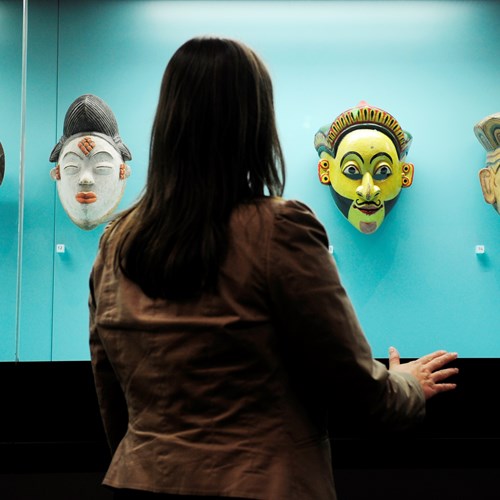 A woman viewing a series of costume masks in the Performance Lives gallery