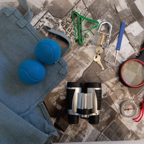 Blue tennis balls, binoculars, magnifying glass, compass and lock and key lie beside blue satchel bag.