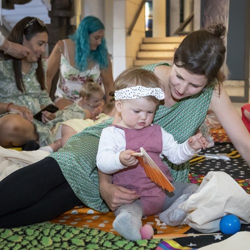 A group of four adults with babies sitting in the museum, taking part in a Magic Carpets session