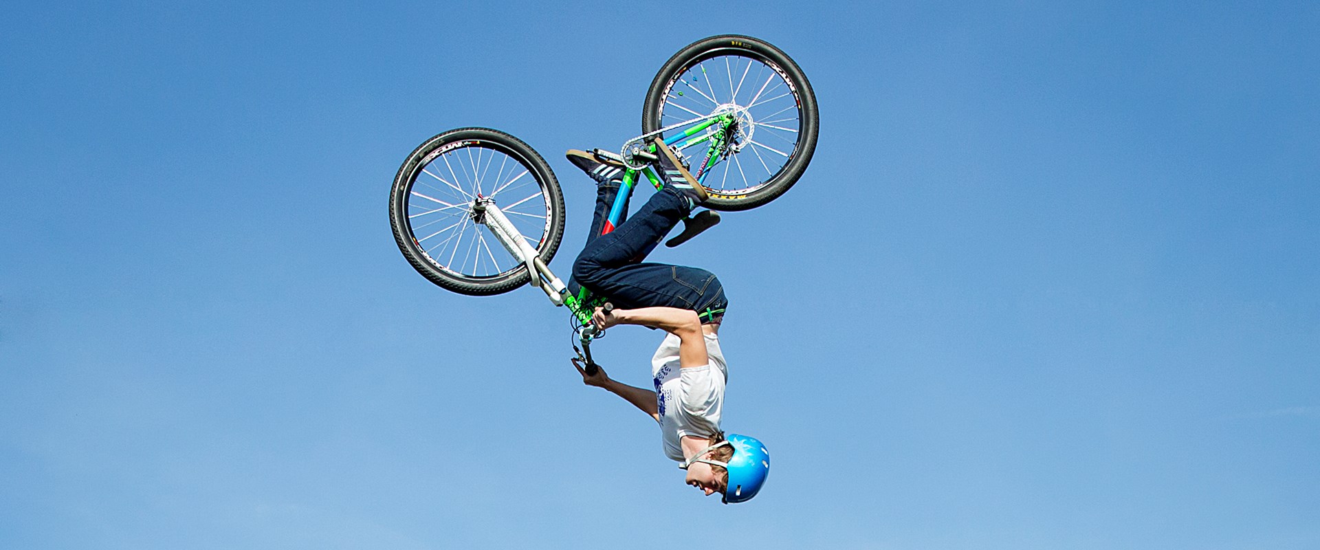 A cyclist in a blue helmet spins upside down against a blue sky.