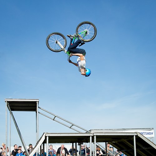 A cyclist in a blue helmet spins upside down against a blue sky.