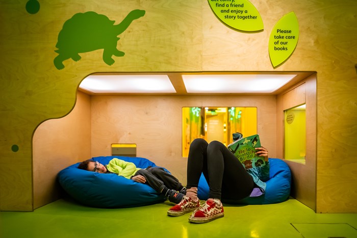 Two children sitting on bean bags in a quiet space. One child is reading a book.