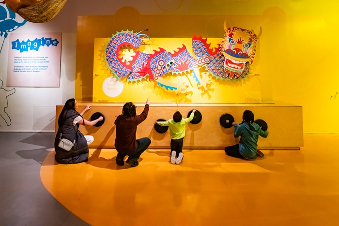 A group of visitors interact with a large display of a Chinese dragon.