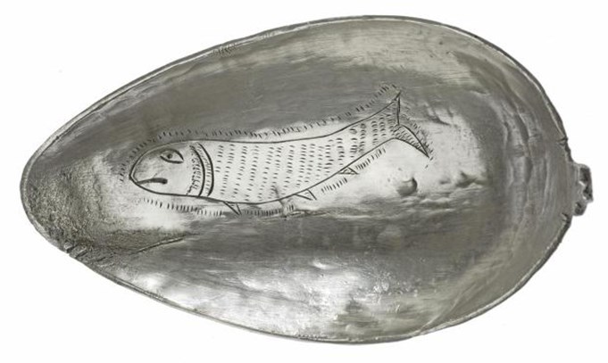 Egg-shaped silver spoon decorated with a scaly fish that looks to be frowning.