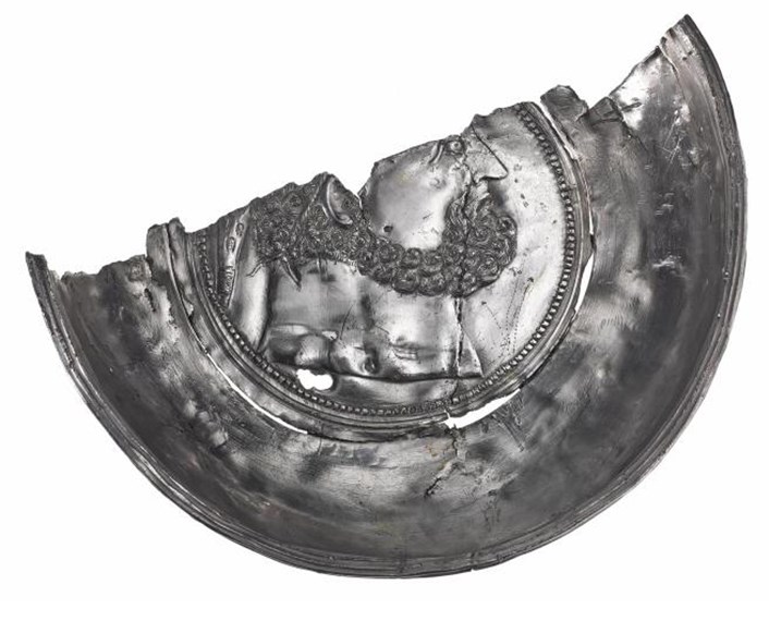 Bottom half of a silver dish cut diagonally across. Bearded, muscle-bound bust of Hercules in the centre.
