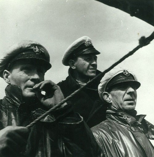 Black and white close-up photo of three men in hats and waterproofs.