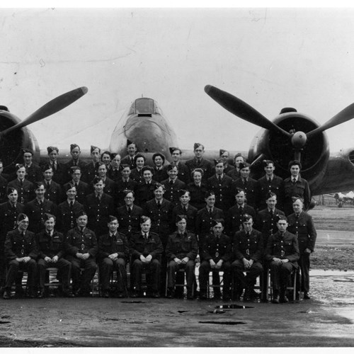 Black and white photo of a group of soldiers in front of a plane on the airfield.