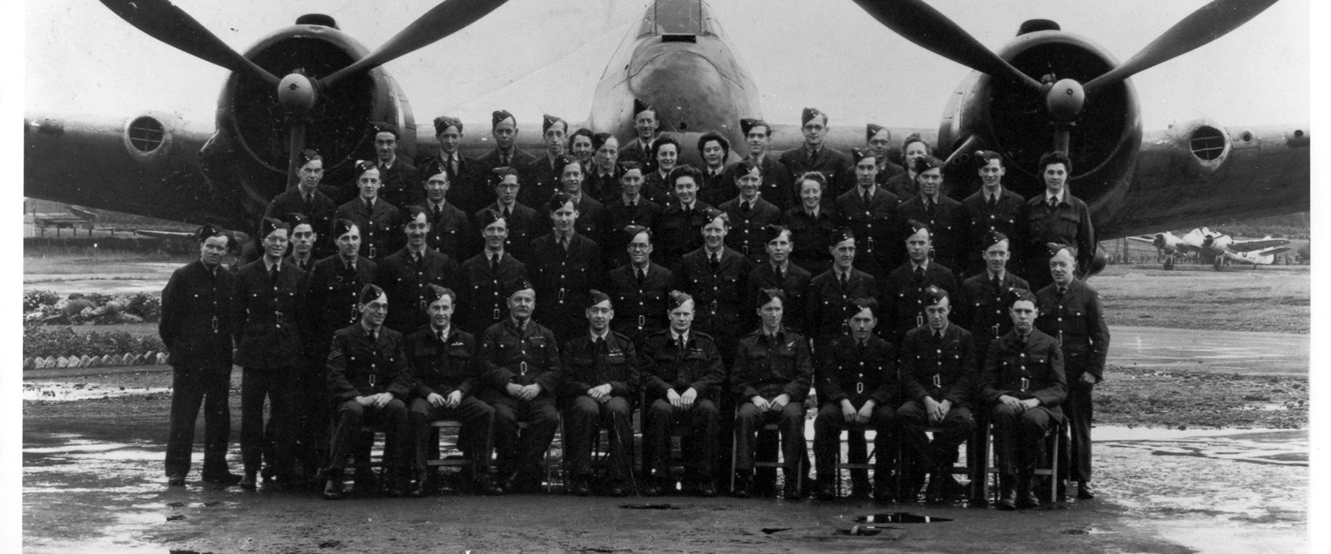 Black and white photo of a group of soldiers in front of a plane on the airfield.