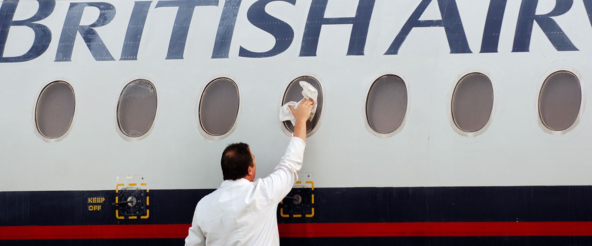A man reaches up to clean the outside of a passenger window of a British Airways plane.
