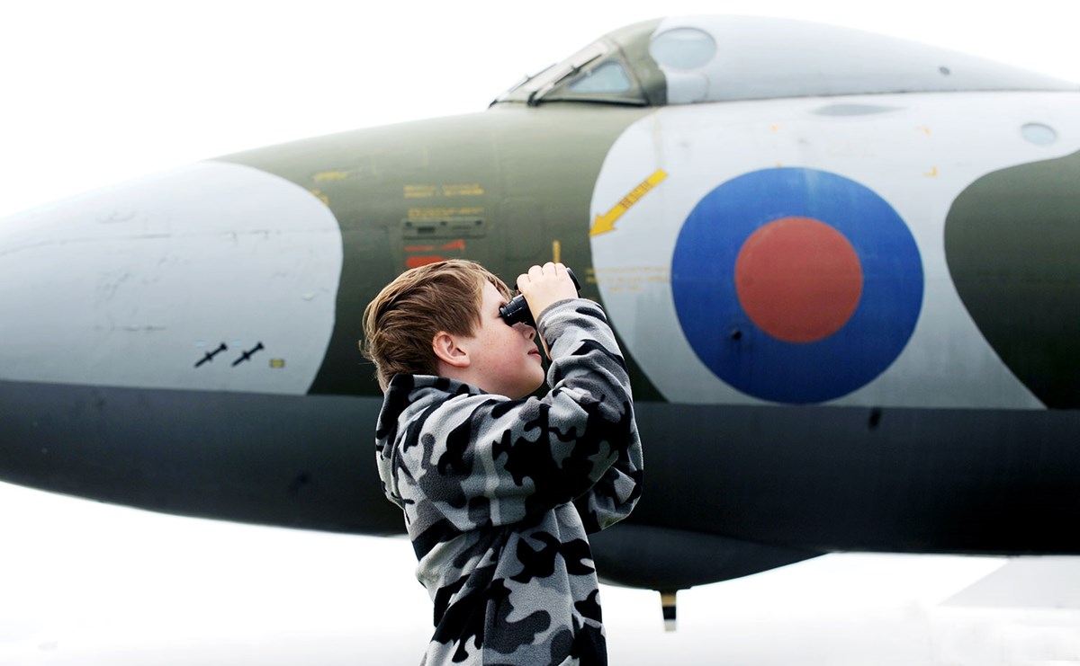 Child standing in front of a plane looking through binoculars.
