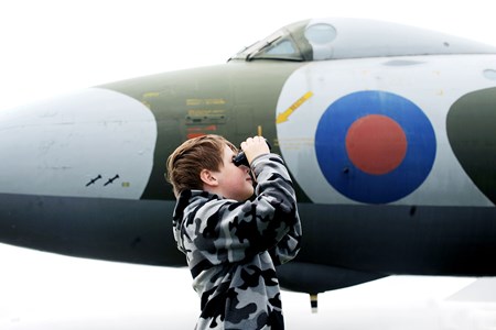 Child standing in front of a plane looking through binoculars.