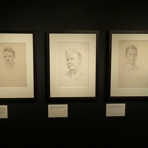 Three hand drawn portraits of First World War soldiers side by side on the wall of a dark gallery space.