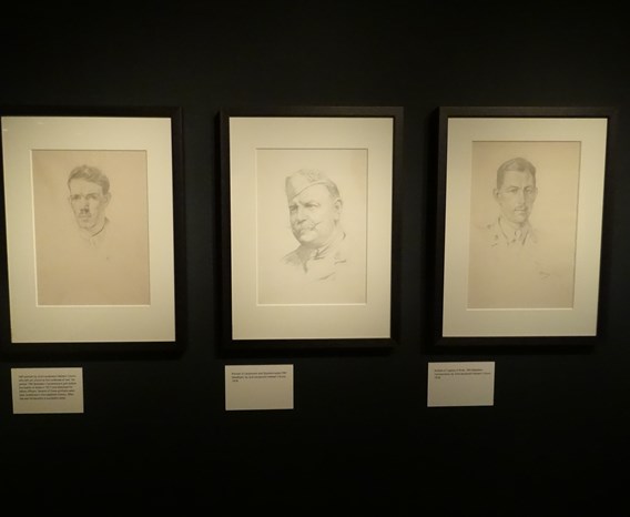 Three hand drawn portraits of First World War soldiers side by side on the wall of a dark gallery space.