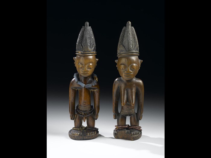 Late 19th-early 20th century male and female ere ibeji figures made from carved and painted wood, wearing high headdresses and strings of beads. Made in Nigeria.