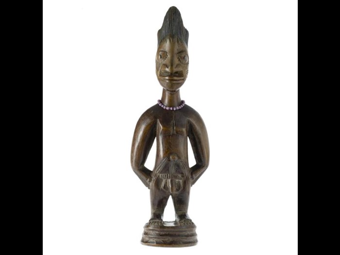 Male ere ibeji figure made from carved wood, with traces of red pigment on the body, and necklace of black and pink glass beads. Made in southwestern Nigeria.