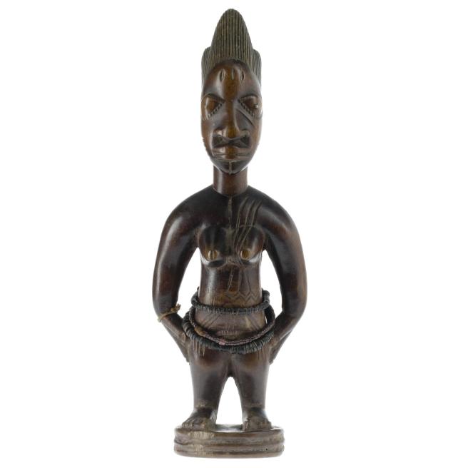 Female ere ibeji figure made from carved wood, with traces of red pigment on the body, and necklace of black and pink glass beads. Made in southwestern Nigeria.