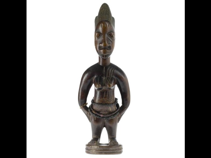 Female ere ibeji figure made from carved wood, with traces of red pigment on the body, and necklace of black and pink glass beads. Made in southwestern Nigeria.