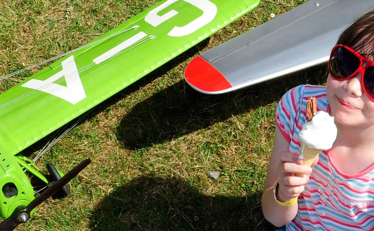 Young child wearing a pair of sunglasses and eating an ice cream cone, standing next to some plane toys.