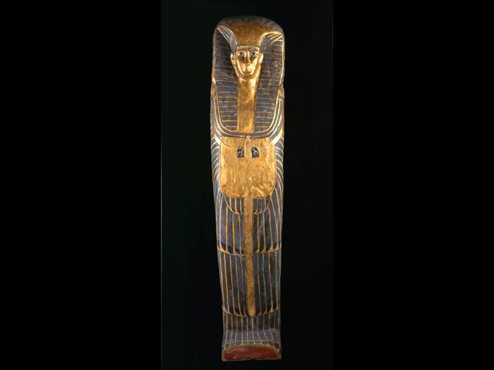 Female coffin: an exceptionally tall coffin with decoration in the rishi-style. The lid has feathered patterning painted in blue with black details on a yellow ground. The owner’s face is framed by a striped linen nemes-cloth, a beaded collar with falcon terminals, and a vulture-pectoral.