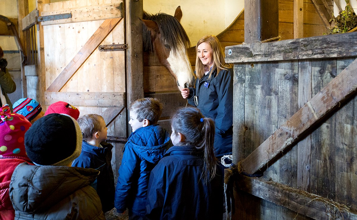 A museum employee stands with a horse in its stable in front of a group of school children
